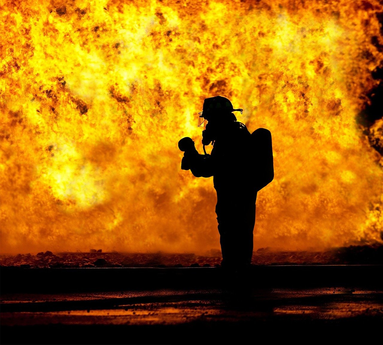 on aperçoit la silhouette d'un sapeur pompier face à un brasier de flamme